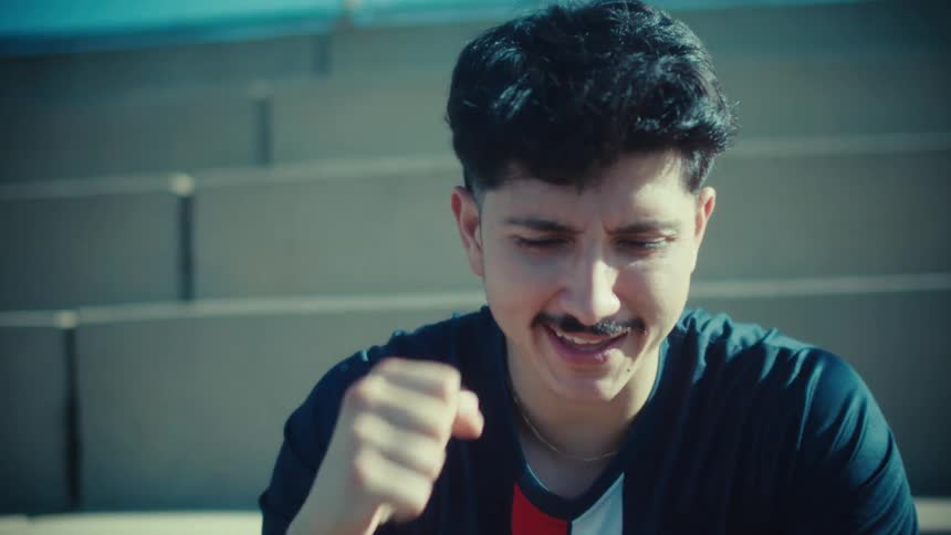 A young soccer player in a USA jersey celebrates winning a mobile game while sitting on the bleachers
