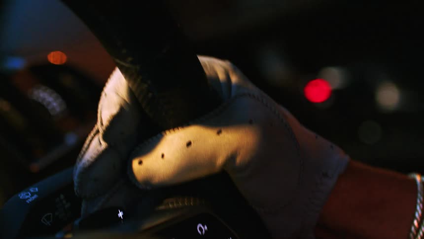 A close-up shot of a hand in a white leather driving glove holding the steering wheel of a car at night