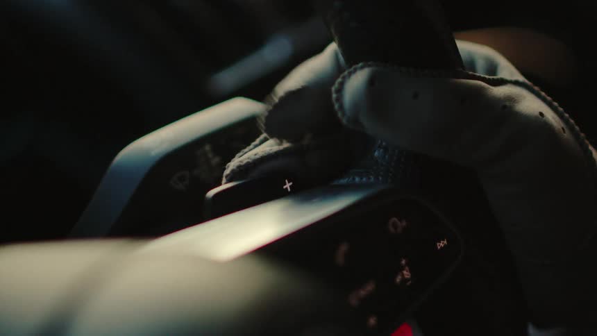 A cinematic close-up of a gloved hand resting on the steering wheel of a modern car
