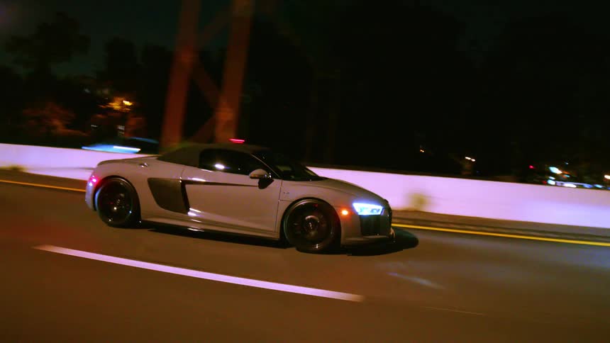 Side profile tracking shot of a grey luxury convertible sports car cruising along a highway at night