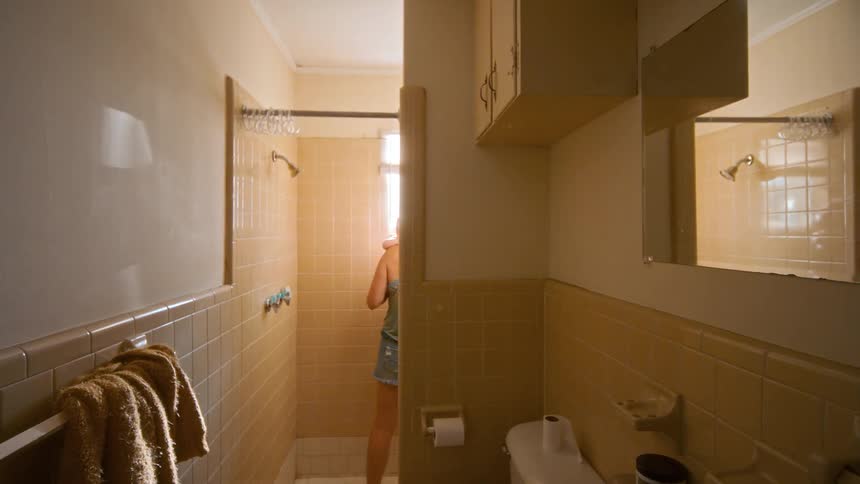 Over-the-shoulder shot reveals a mother comforting her baby while walking into the shower
