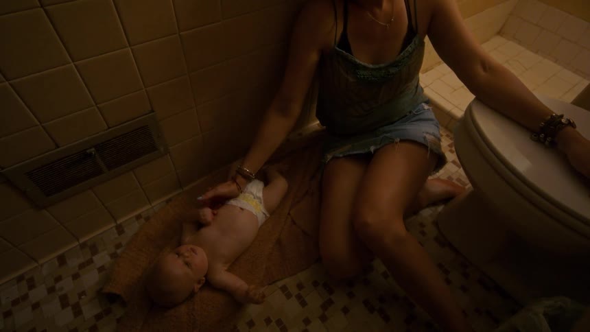 An exhausted young mother collapses on the floor of a dingy bathroom next to her newborn baby