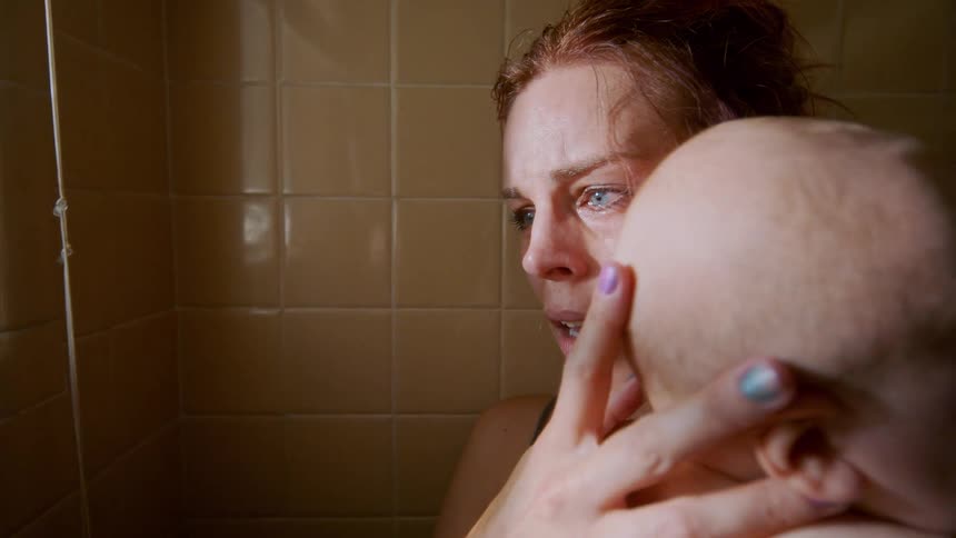 A terrified and tearful mother clutches her baby tightly in a dark bathroom, overcome with anguish and fear as she closes the blinds