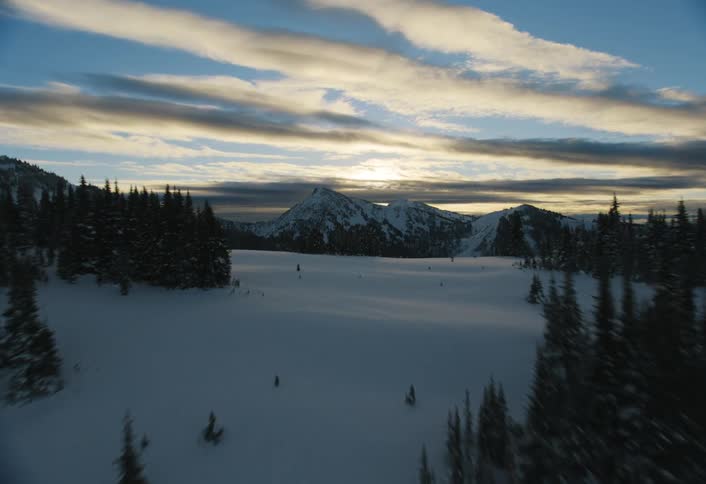 An awe-inspiring aerial view flying over a snow-covered forest towards distant mountain peaks at sunrise