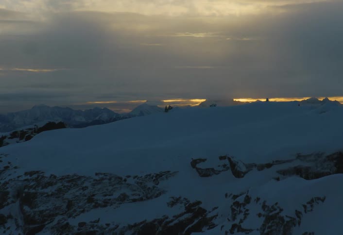 An aerial reveal shot of a vast snowy mountain range as the sun rises on a cloudy morning