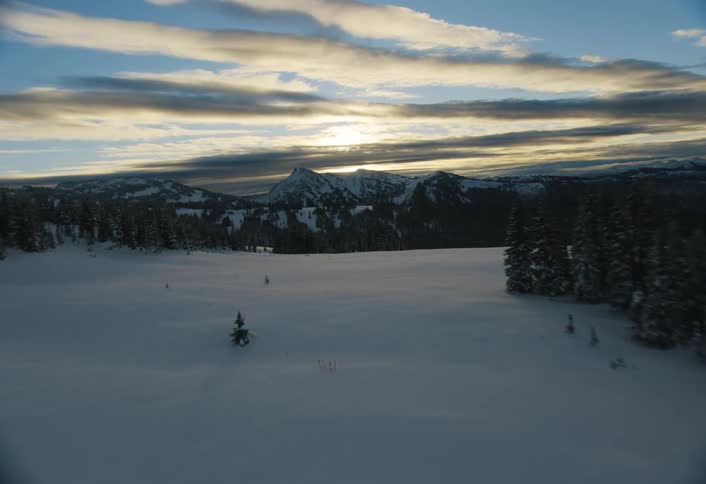 A majestic aerial flight over a vast, snow-covered forest towards a distant mountain range at sunrise