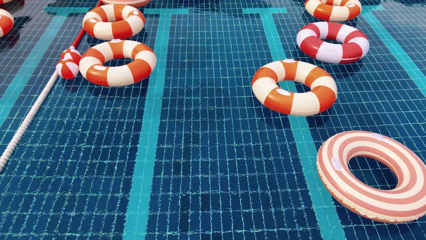 A variety of striped inflatable rings gently bob on the rippling surface of a bright blue swimming pool