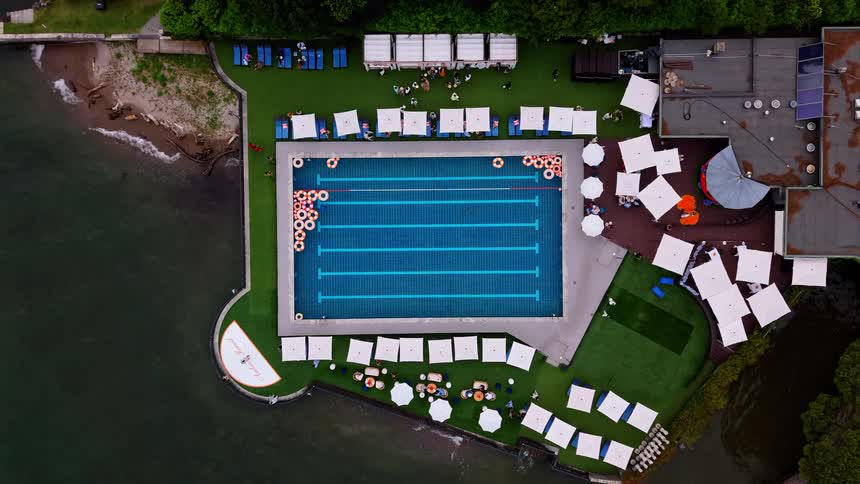Aerial top-down timelapse of a luxury resort swimming pool next to the ocean with people lounging and floaties drifting in the water