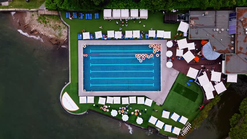 An aerial time-lapse view of a busy luxury swimming pool party at a beautiful waterfront resort