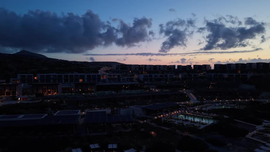 A slow aerial push-in shot reveals a luxurious seaside resort beautifully illuminated at dusk