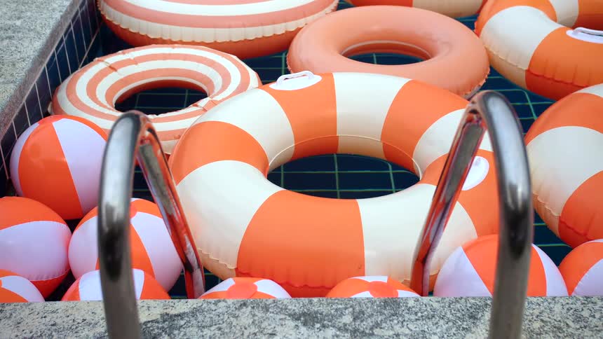 A pool filled with orange and white inflatable rings and beach balls as seen through a pool ladder