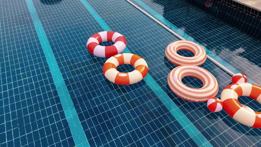 Colorful red and orange striped inflatable rings float gently in a serene blue tiled swimming pool