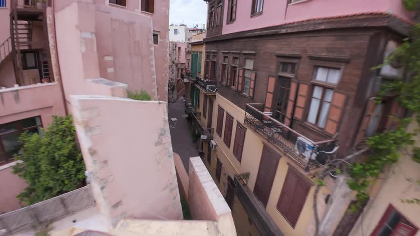 A slow aerial pullback reveals a picturesque, narrow cobblestone street nestled between colorful, historic buildings in an old European city