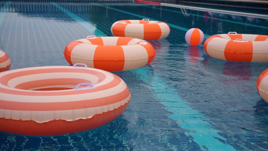 Inflatable orange and white pool floats bob in the clear blue water of a swimming pool during a light rain shower