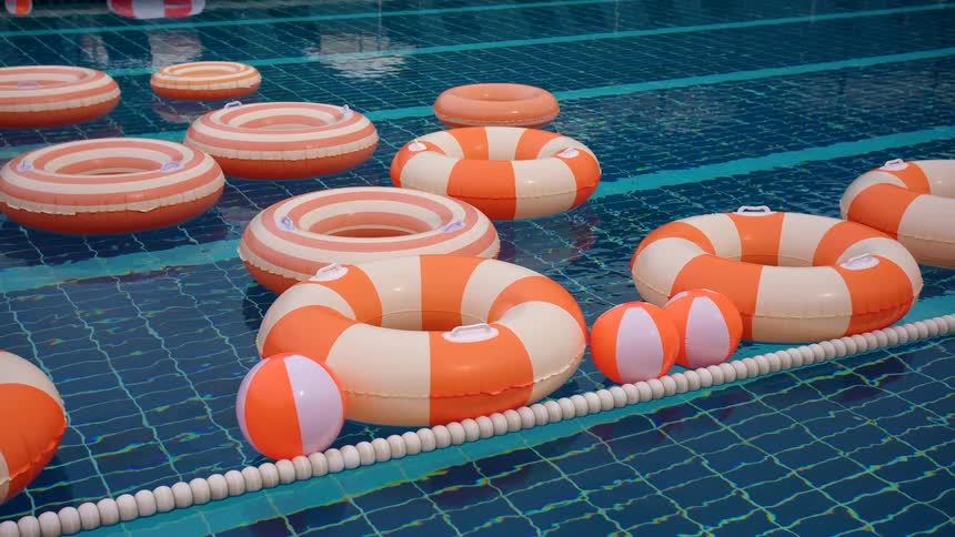 Empty swimming pool filled with orange and white striped inflatable rings and beach balls