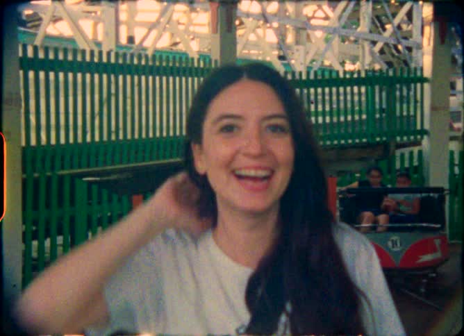 Vintage film footage captures a joyful young woman smiling and making a peace sign on a spinning amusement park ride