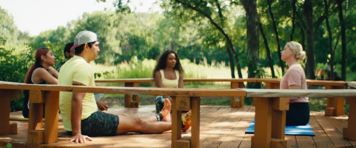 A female instructor leads a mindful discussion with a diverse group of people sitting in a circle on an outdoor deck