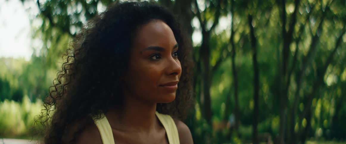 Close-up profile of a serene woman with curly hair finding a moment of peace and happiness in a lush green park