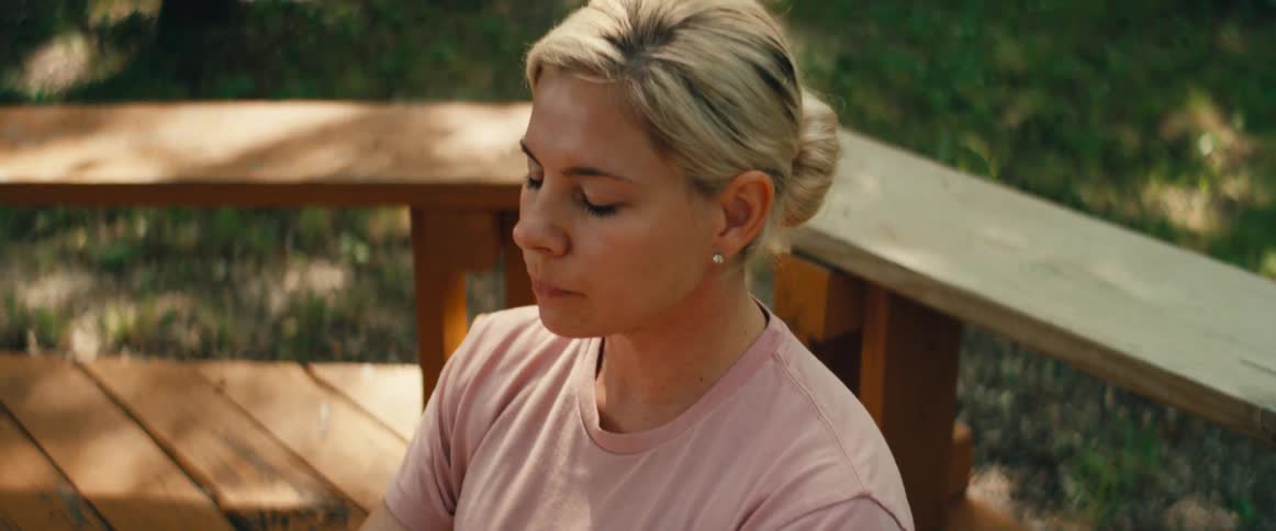 A serene blonde woman meditates peacefully on a blue yoga mat on an outdoor wooden deck
