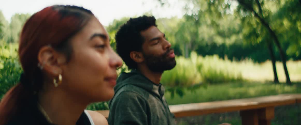 A young man and woman find a moment of peace and tranquility as they meditate together outdoors in a lush, green park