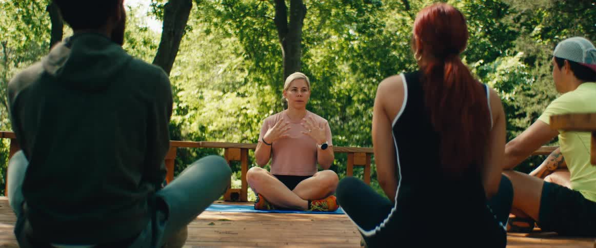 A focused yoga instructor guides a small class through a meditation session on a peaceful outdoor wooden deck