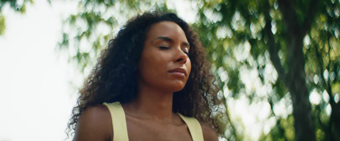 A serene woman with curly hair finds a moment of peace and tranquility while meditating outdoors