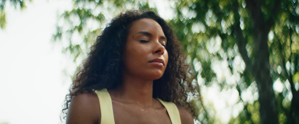 Close-up of a serene woman meditating outdoors, with the camera tilting from her hand to her peaceful face