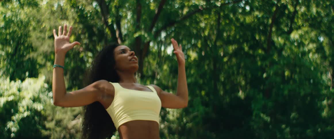 A serene Black woman practices yoga and meditation on a deck, with arms raised towards the sky in a peaceful, natural setting