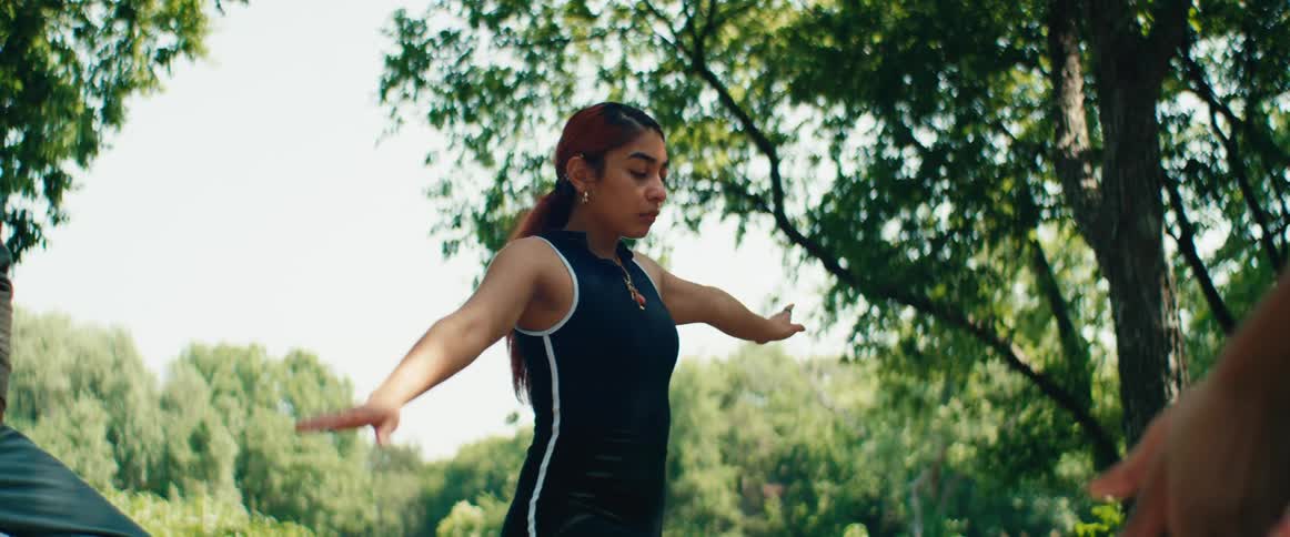 A serene young woman practices a mindful yoga routine, raising her arms slowly in a lush green park
