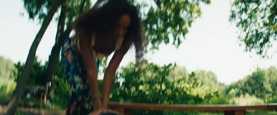 A focused woman with curly hair warms up her hands and prepares for an outdoor activity in a sunny park
