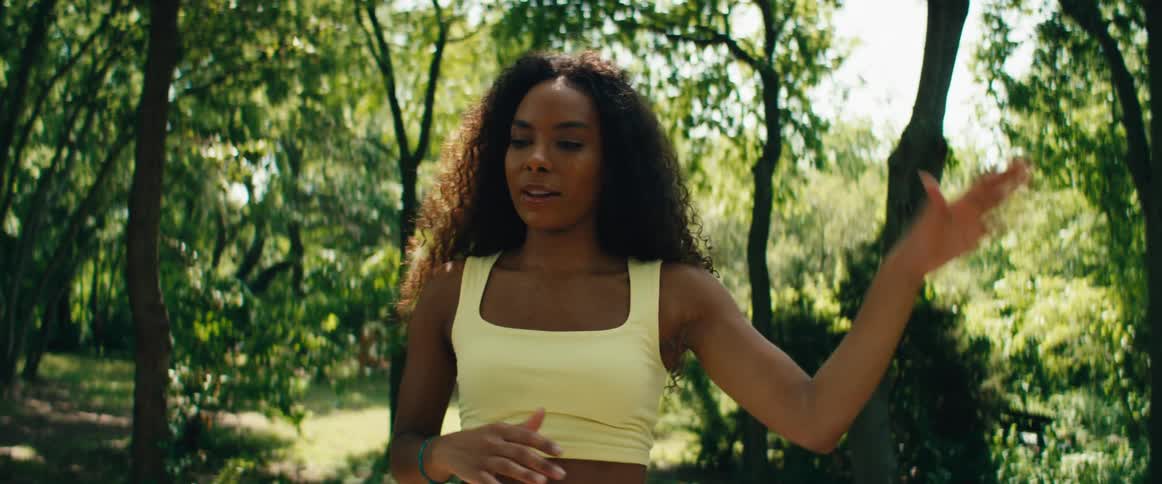 A beautiful, curly-haired woman in a yellow top practices mindful, slow-motion movements in a sunlit park