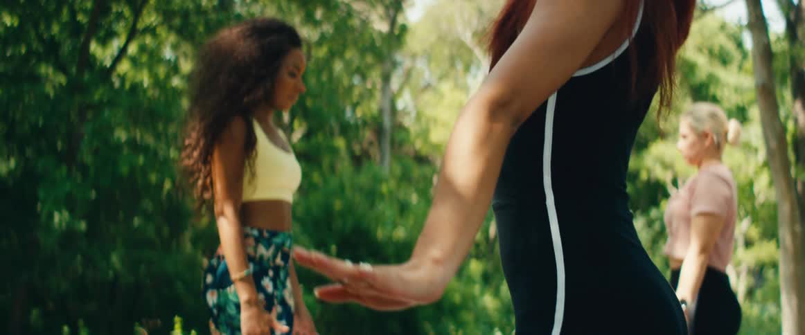 Slow motion side view of a focused woman gracefully moving her arms down during an outdoor yoga class in a sunny park