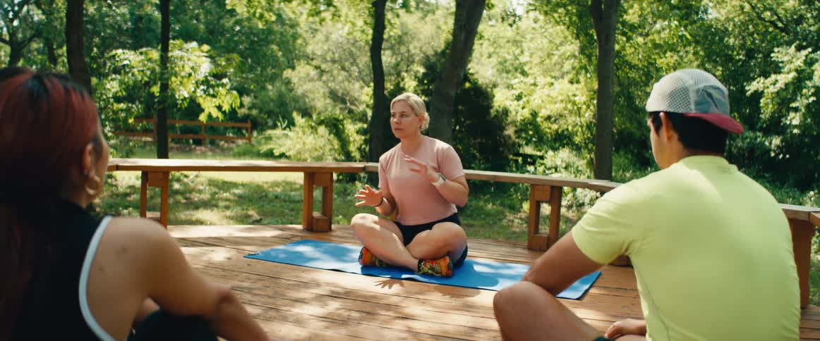 A female instructor leads a meditation and wellness class for a small group outdoors on a sunny wooden deck