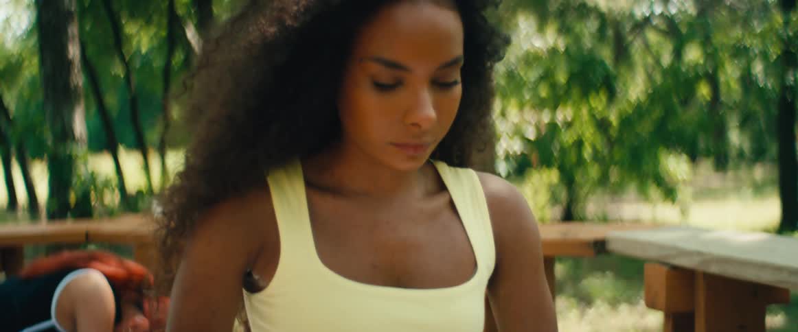 Slow tilt-up shot reveals a focused young woman in activewear performing a deep yoga stretch on a towel outdoors