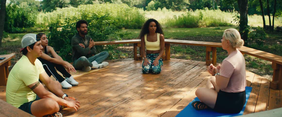 A yoga instructor leads a diverse group in a guided meditation session on a sunny day at an outdoor retreat