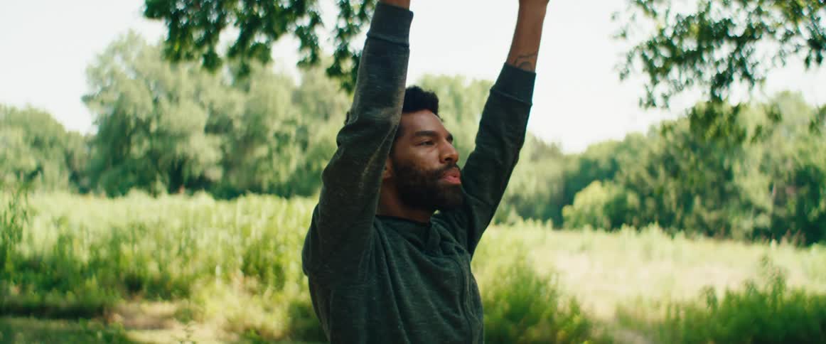 A bearded man with closed eyes stretches his arms to the sky in a moment of tranquil meditation in nature
