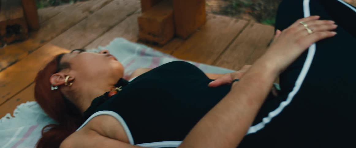 Slow pan of a woman with red hair in athletic wear peacefully resting on a blanket on a wooden floor