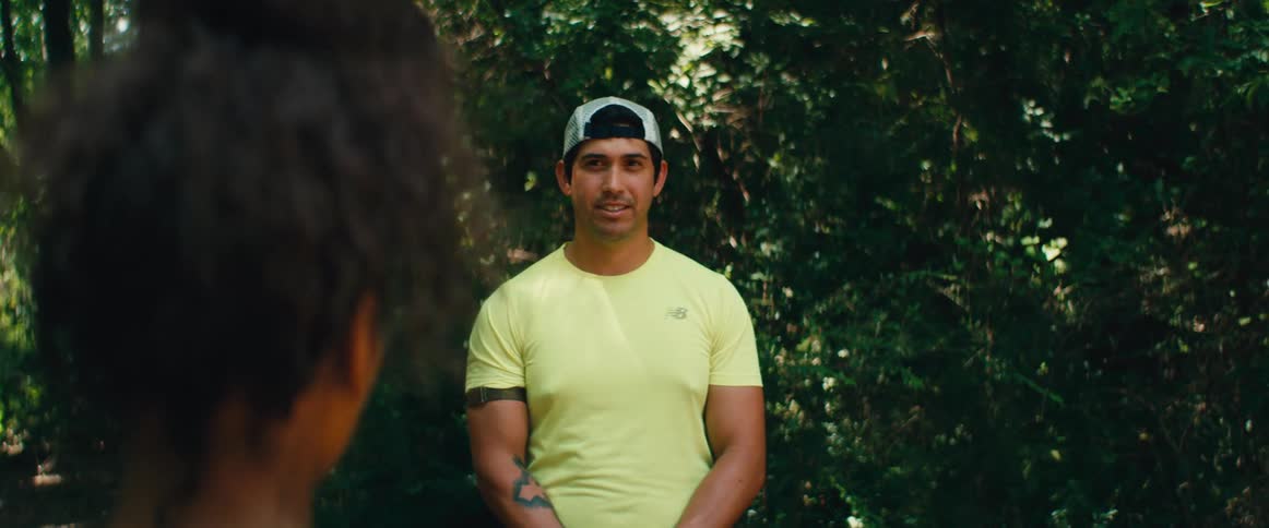 A man in a yellow shirt and a baseball cap has a pleasant conversation and laughs with a friend in a park