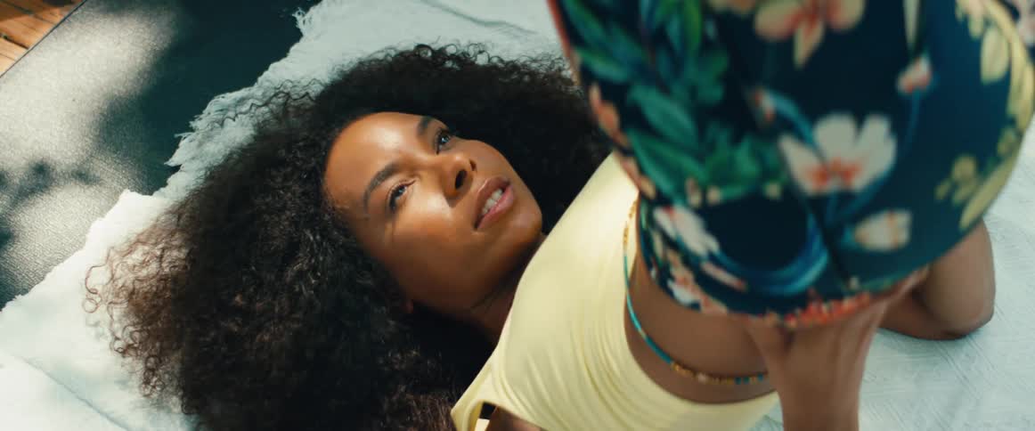A serene woman with beautiful curly hair lies on a blanket outdoors, closing her eyes in a peaceful, intimate moment