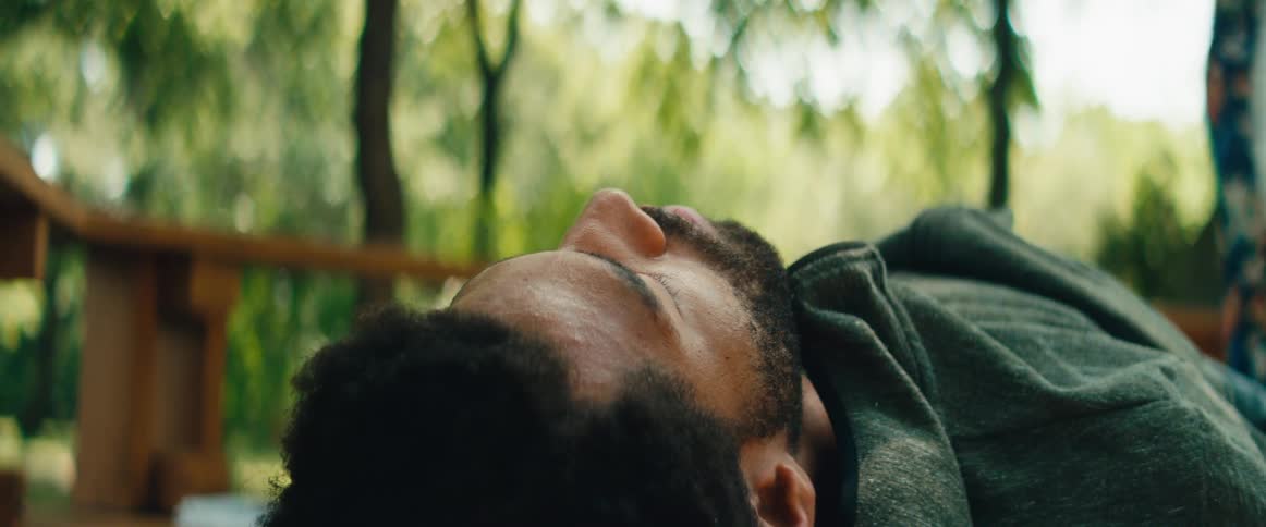 A serene close-up of a man with his eyes closed, resting peacefully in nature as a white feather floats gently past his face