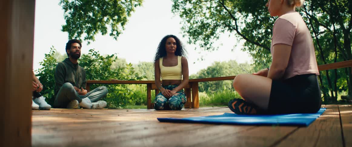 A diverse group of people attend an outdoor yoga and meditation class led by a female instructor in a tranquil park