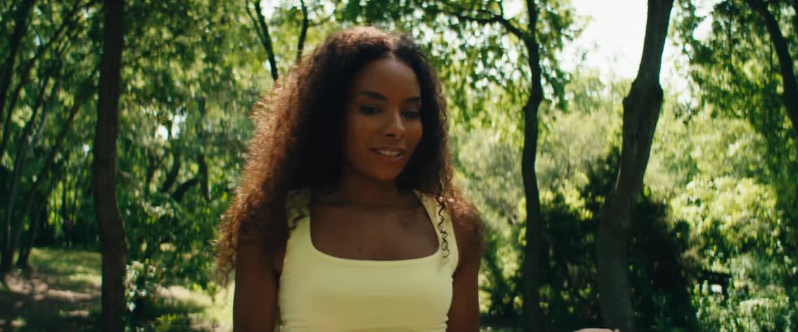 A serene woman with curly hair leads a guided meditation and practices mindfulness in a lush, sunlit park