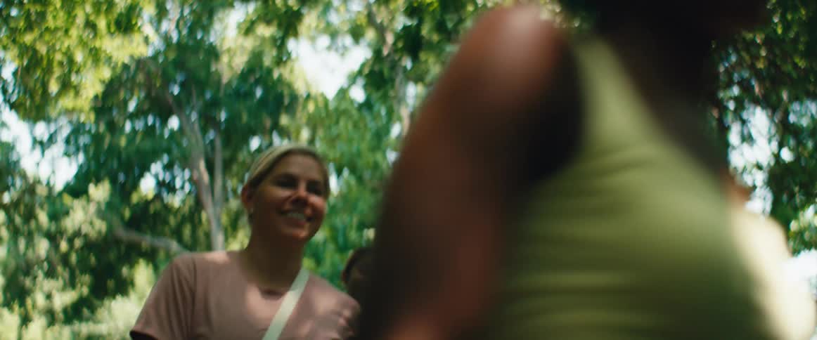A low angle, slow motion shot shows a diverse group of smiling friends walking through a sunlit park