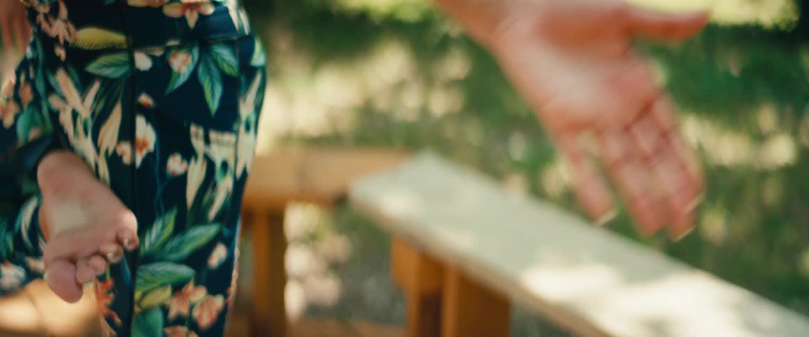 A woman's hand in a meditation mudra slowly rises as she practices yoga in a serene, sunlit park