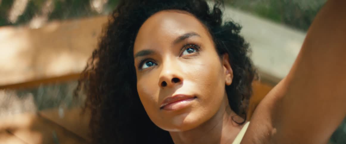A serene close-up of a Black woman with curly hair enjoying a peaceful moment outdoors in the warm sunlight
