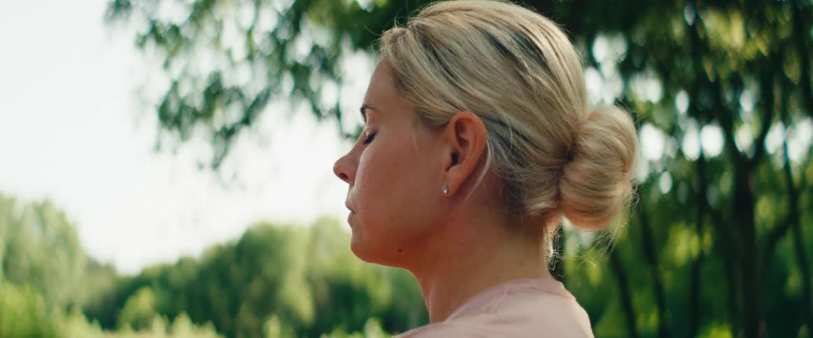 Close up of a serene blonde woman meditating with her eyes closed in a lush green park on a sunny day