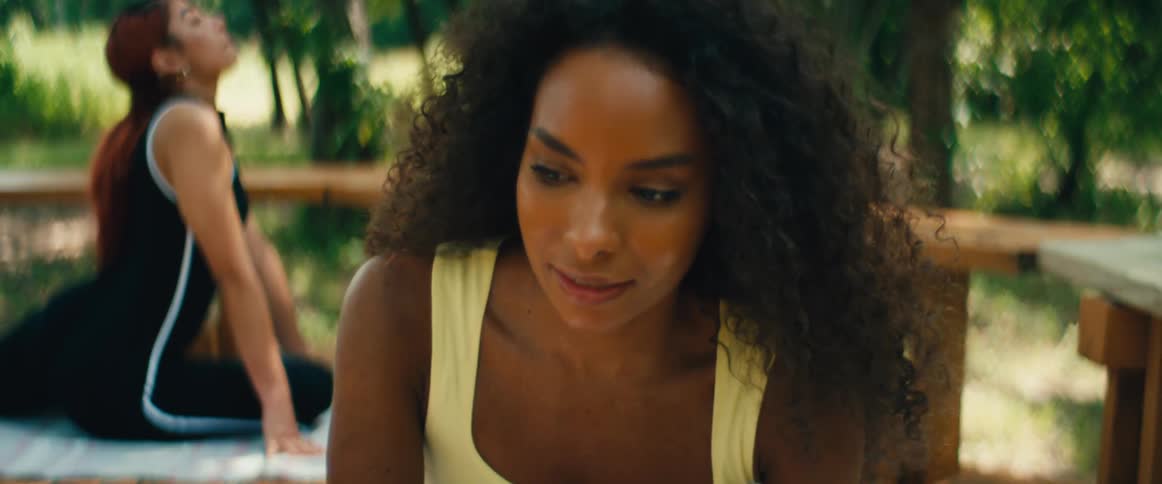 A serene Black woman with curly hair takes a deep breath and centers herself before a yoga session in a sunny park