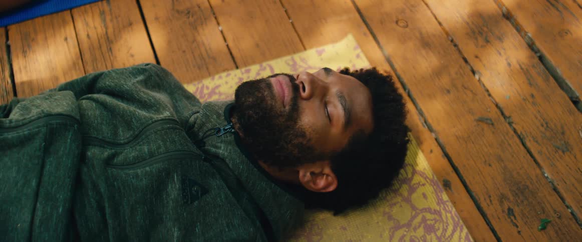 High angle close-up of a man peacefully napping on a yoga mat when a hand enters the frame and playfully pokes his nose