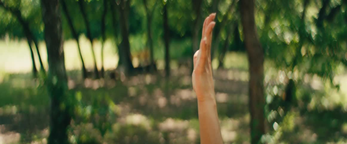 Slow motion, high-angle close-up of a serene woman stretching on a wooden deck in a sunlit forest