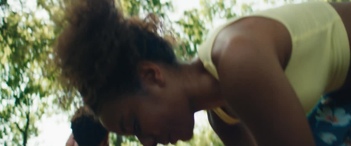 A close-up of a person putting on a dark green athletic shoe and tying the laces while sitting on outdoor wooden steps